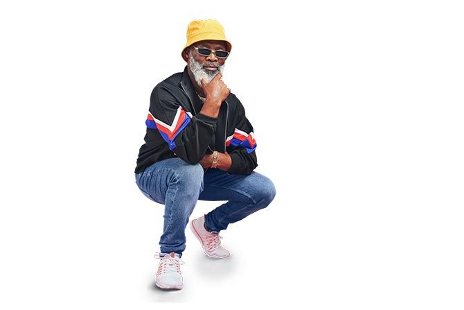Choosing the Right Retirement Plan for Your Small Business; A man in a yellow bucket hat and sunglasses crouches thoughtfully. He's wearing a black jacket with colorful stripes, blue jeans, and white sneakers, exuding a cool, laid-back vibe.