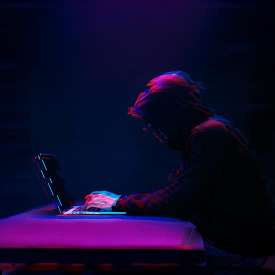 Endpoint-Detection-FEATURE - Person in a dark hoodie typing on a laptop with a glitching purple and blue light effect around them