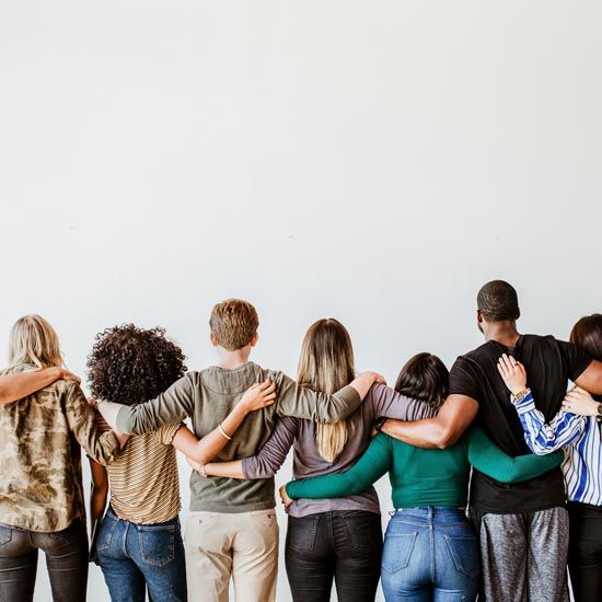 Flourish-FEATURE - Group of younger adults facing away from the camera with arms interlocked around each other's backs.